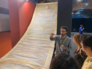 Gianluca Bosi ieri al Meeting di Rimini mentre spiega il suo papiro di nove metri in cui ha scritto tutta la bibbia, in latino